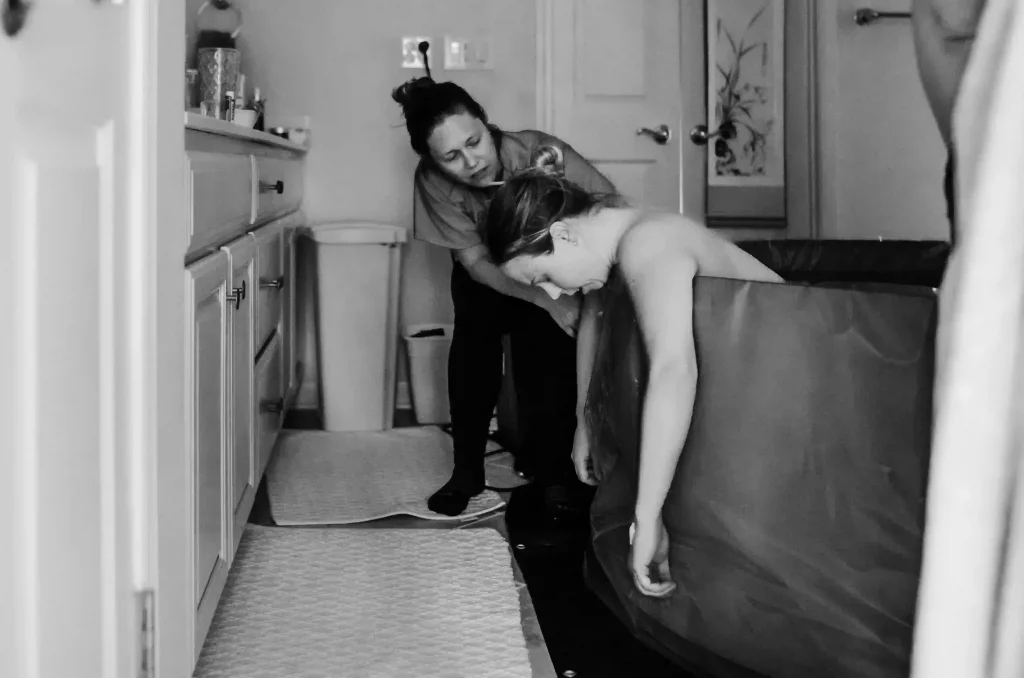 Femme dans une baignoire gonflable en train d'accoucher à domicile assisté d'une sage-femme.